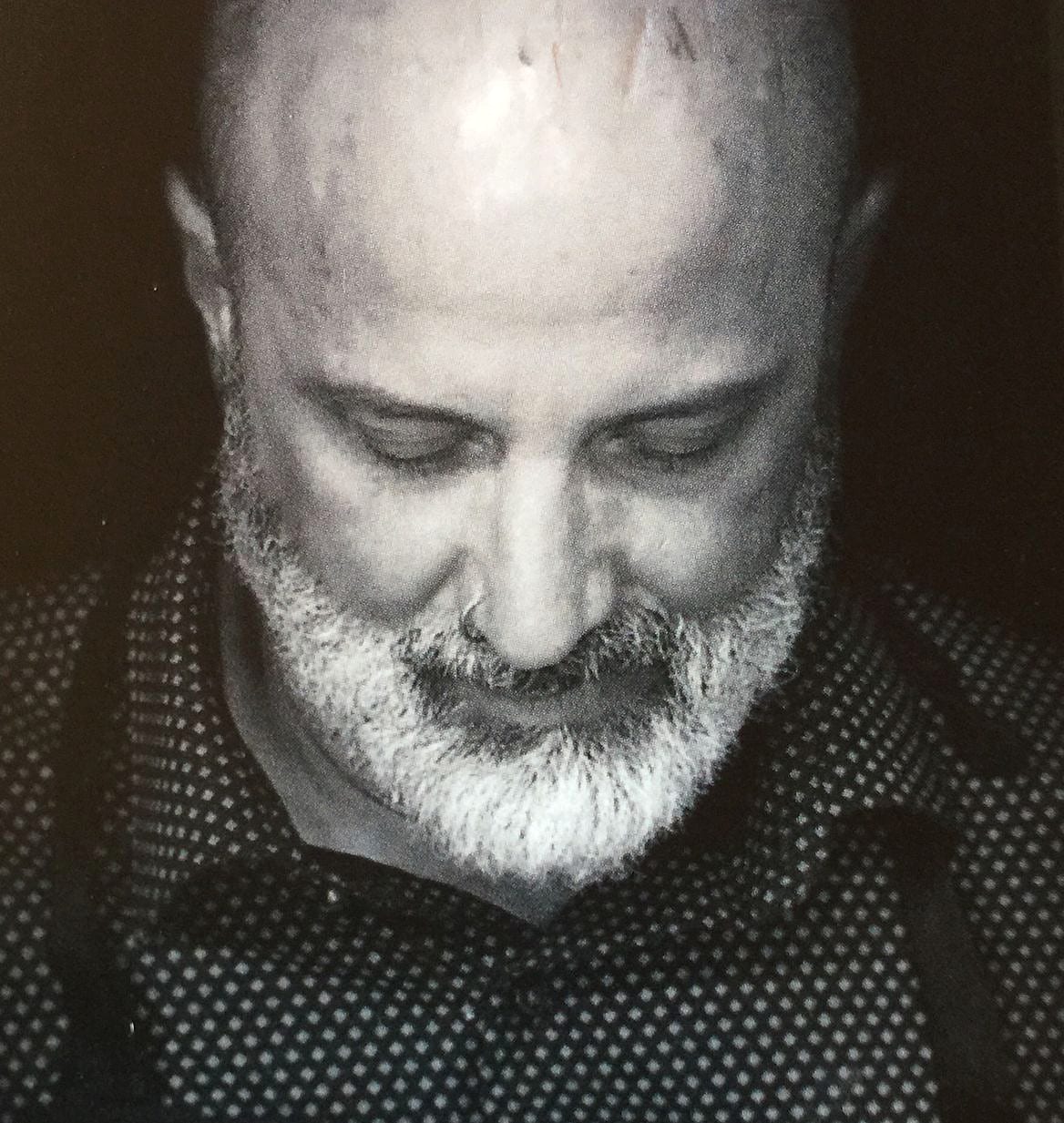 Black and white portrait of a bearded man in a patterned shirt looking downward